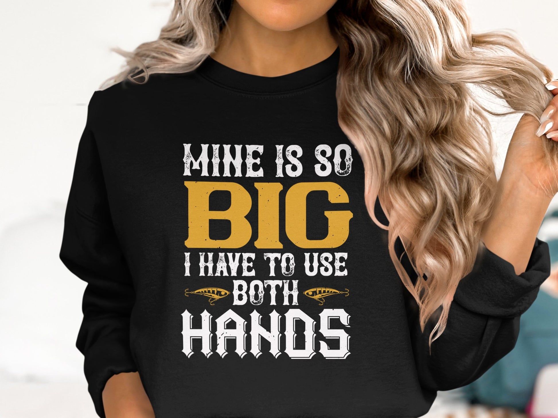 A person with long, wavy blonde hair is wearing a distinctive sweatshirt from Garment Graphics with the bold statement: MINE IS SO BIG I HAVE TO USE BOTH HANDS, embellished with decorative accents.