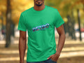 A person is outside in a vibrant green T-shirt with a Retro Graphic Design by Garment Graphics. The backdrop shows blurred trees and fallen leaves, giving the park or natural setting a vintage charm.