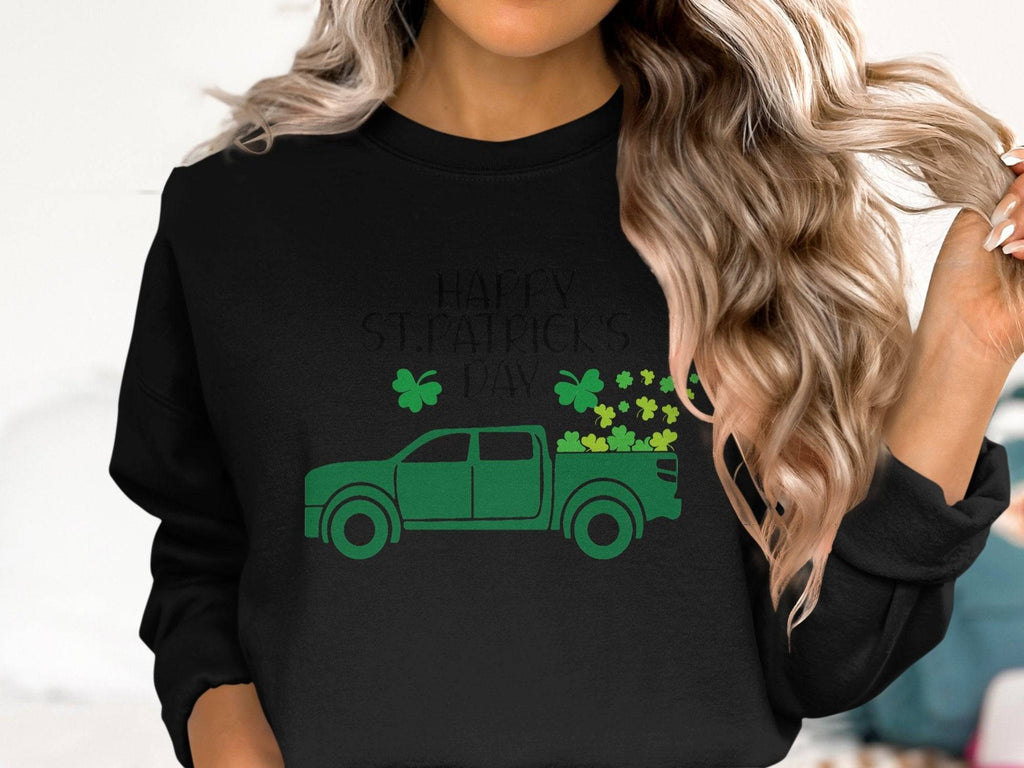 A woman with long, wavy blonde hair wears a festive Garment Graphics sweatshirt featuring a green truck adorned with shamrocks and the message Happy St. Patricks Day.