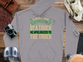 Garment Graphics presents a witty gray hoodie featuring the quote: If an Englishman gets run over by a truck, he apologizes to the truck, styled on wood alongside a camera, notebook, binoculars, and gloves.