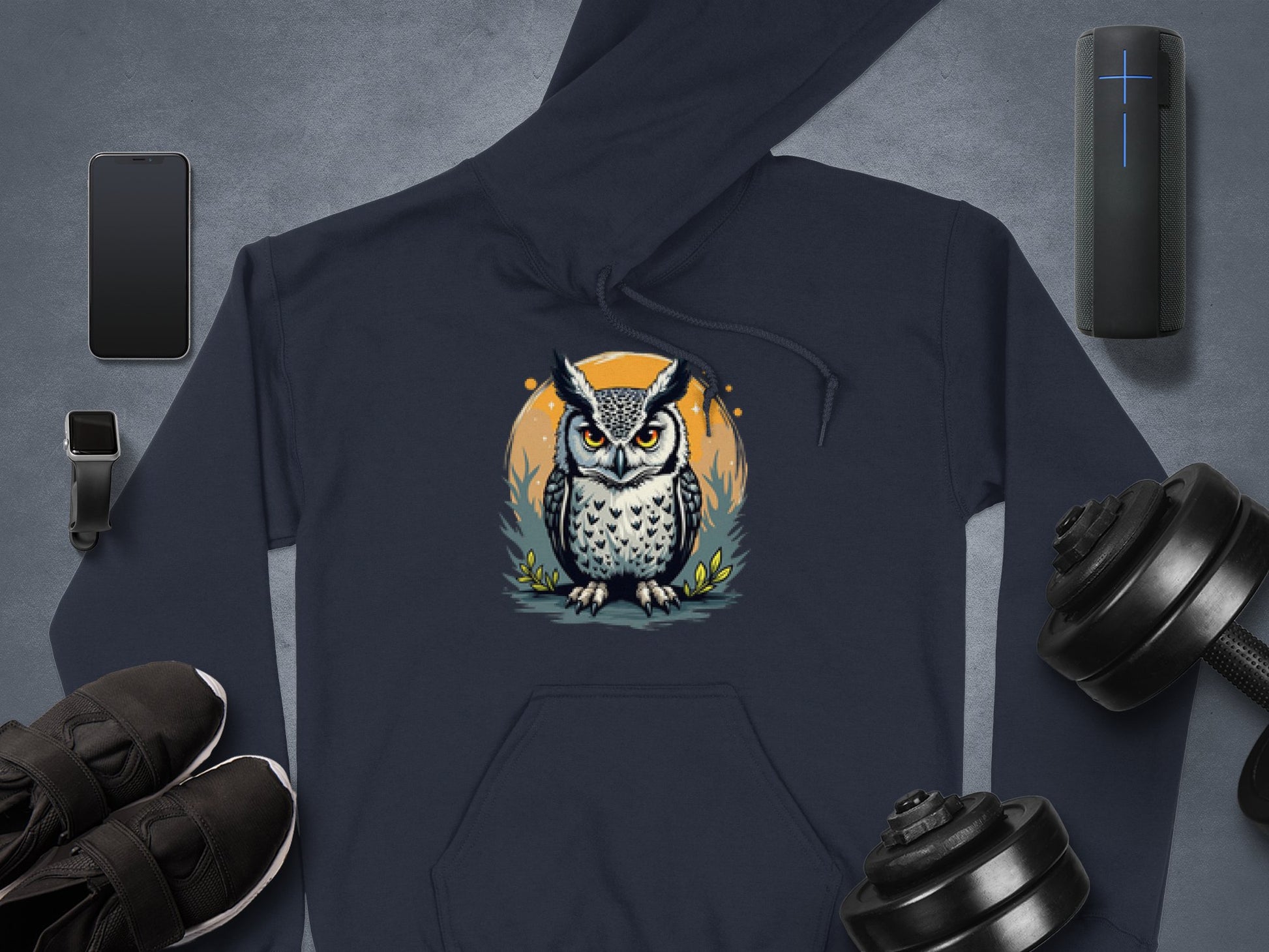 Explore the distinct style of Garment Graphics navy blue hoodie with a bold owl design against a bright yellow moon. Paired with essentials like a smartphone, smartwatch, sneakers, wireless speaker, and dumbbells on a sleek gray surface. Crafted from medium-heavy fabric for lasting comfort.