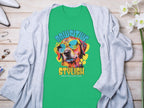 The Garment Graphics Dog T-shirt showcases a dog in sunglasses with the phrase Chillin Like A Canine Villain. Styled on wood, its paired with a light gray cardigan, white flowers, perfume, rings, and white pointed shoes for a paw-sitive stylish vibe.