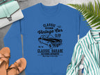 The Garment Graphics blue Vintage Car Sweatshirt features a Classic Vintage Car Club graphic with a car illustration and text: Classic London City, Classic Garage, and Old School Automotive. Nearby are shoes, a purse, and a striped shirt on the gray surface.