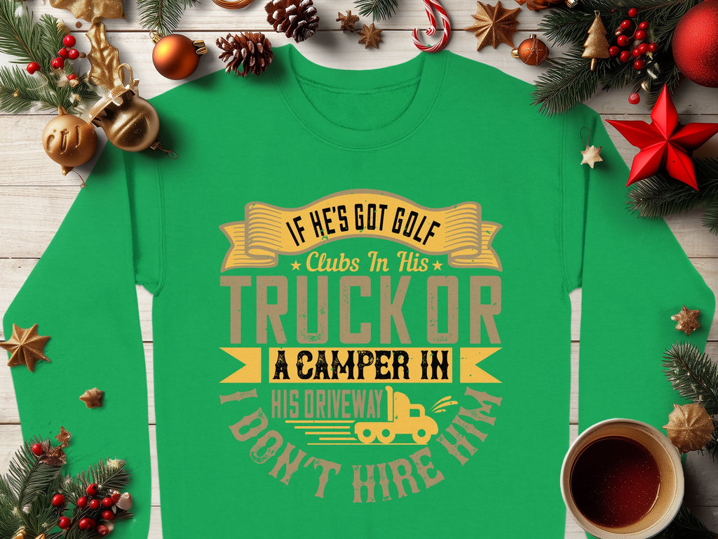 Amid festive decor like pinecones and ornaments, a cozy cup of coffee sits beside Garment Graphics green sweatshirt. It declares: If hes got golf clubs in his truck or a camper in his driveway, I dont hire him. Ideal for those who enjoy humor with an outdoorsy vibe.