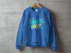 A blue Garment Graphics unisex sweatshirt, featuring a Take It Easy graphic with colorful letters, arrows, and musical notes, hangs on a wooden hanger against a concrete wall—ideal for your casual wear collection.