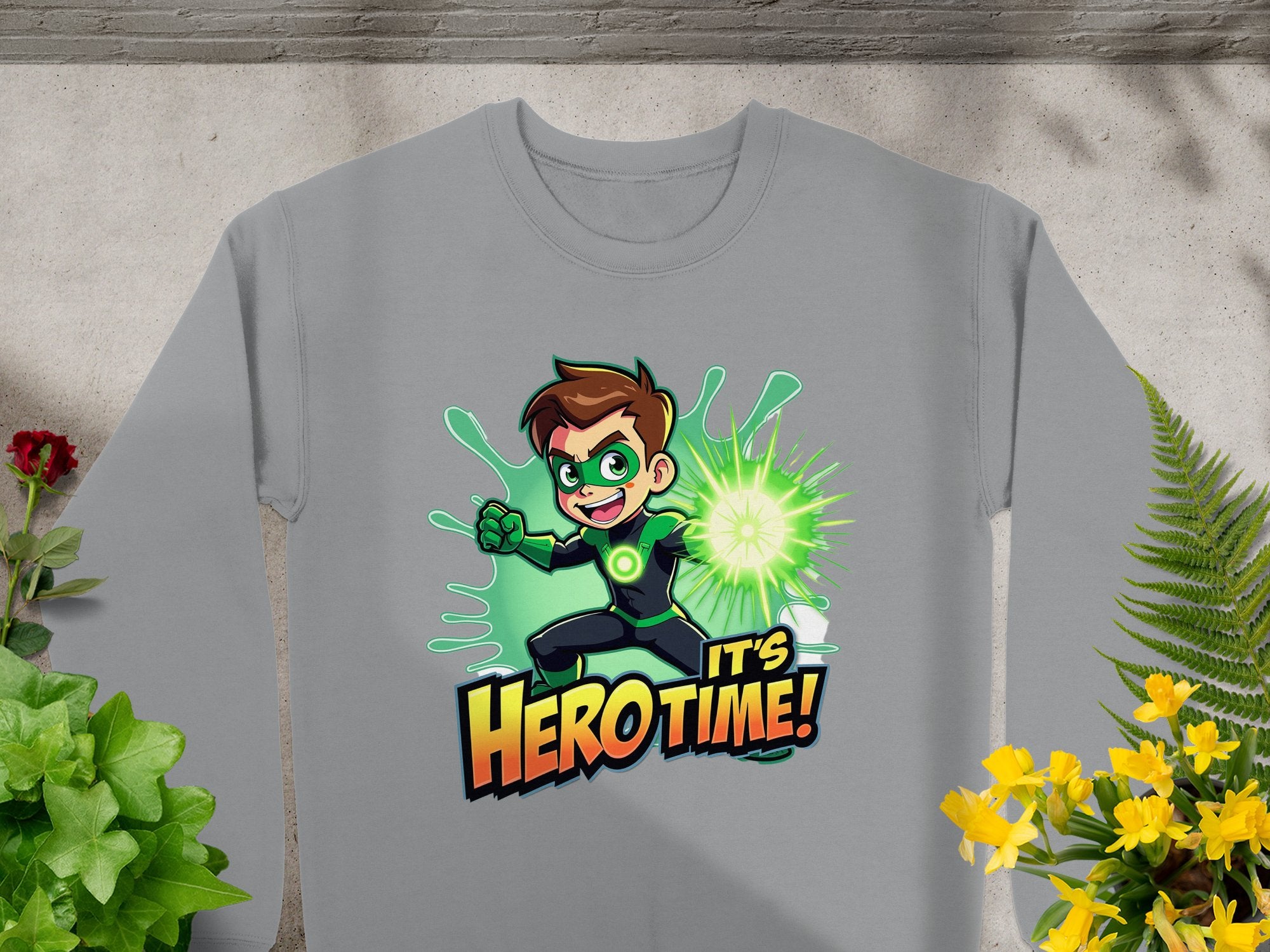 The Garment Graphics gray sweatshirt showcases a cartoon superhero with brown hair in a green suit, emitting green energy. The text Its Hero Time! is below. Decorated with vibrant plants and flowers, this unisex piece is perfect for fans of the genre.