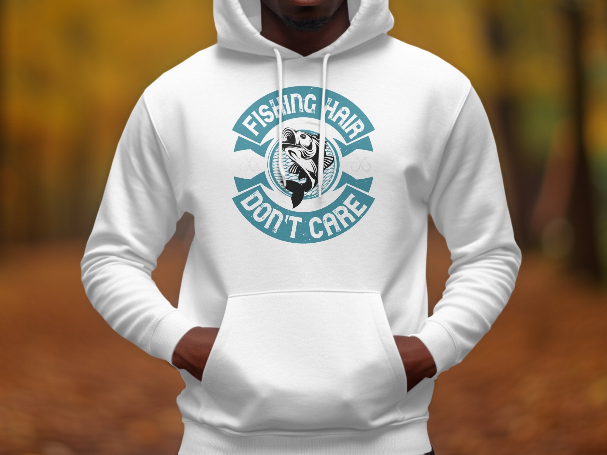 A person wears a Garment Graphics white hoodie featuring an anglers catch design and Fishing Hair Dont Care in teal, set against a blurred outdoor backdrop with trees and leaves.