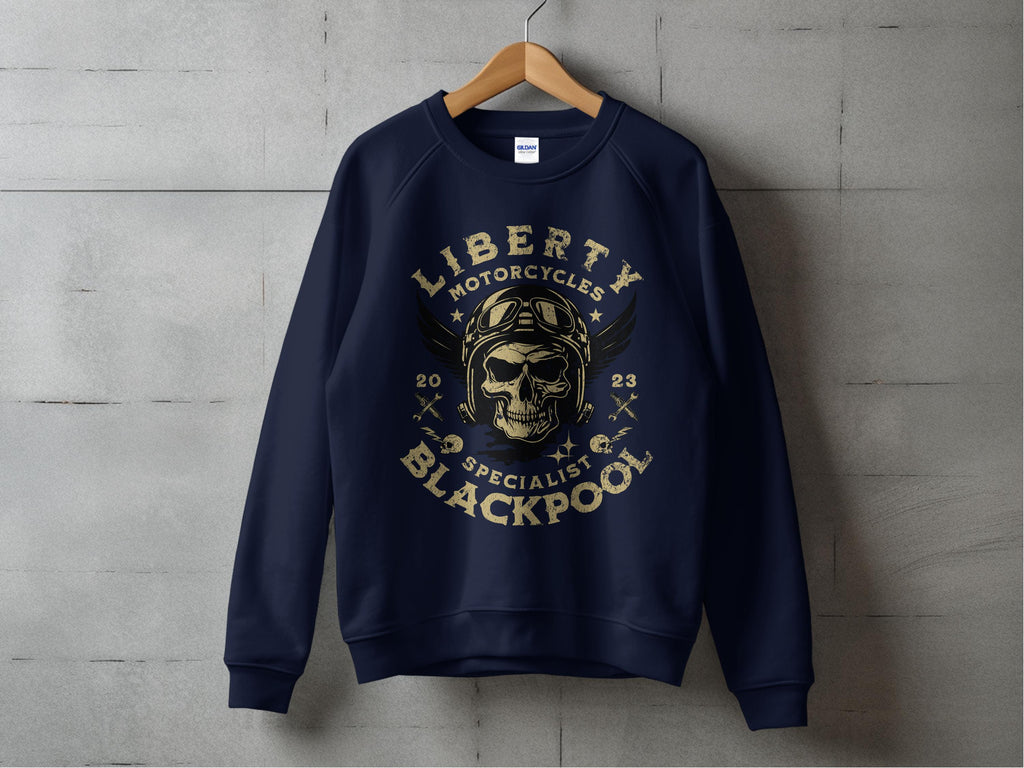 A dark blue sweatshirt by Garment Graphics hangs on a wooden hanger against a gray background, featuring a skull in goggles and helmet graphic, framed by Blackpool 2023 Sweatshirts - Liberty Motorcycles Specialist.