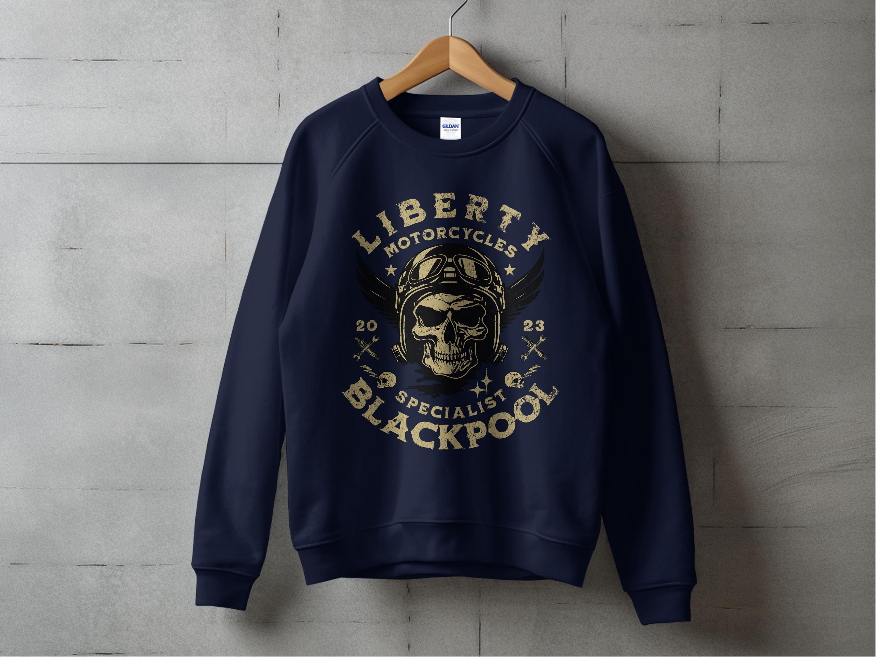 A dark blue sweatshirt by Garment Graphics hangs on a wooden hanger against a gray background, featuring a skull in goggles and helmet graphic, framed by Blackpool 2023 Sweatshirts - Liberty Motorcycles Specialist.