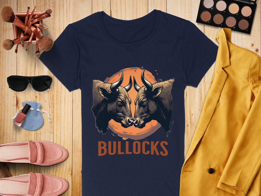 A navy T-shirt from Garment Graphics, adorned with bold bull illustrations and BULLOCKS, is laid out on a wooden surface. Its paired with makeup brushes, eyeshadow, sunglasses, a yellow jacket, pink shoes, and nail polish—ideal for creating a casual wear vibe.