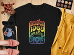A retro black sweatshirt by Garment Graphics features a colorful Woodstock 1969 design with a car and flowers, surrounded by makeup brushes, palette, sunglasses, coin pouch, nail polish, pink loafers, and mustard yellow blazer.