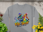 This stylish gray sweatshirt by Garment Graphics showcases two street dancers in colorful outfits, with bold Risk Taker Street Dance 10th Final text. Laid on concrete, its surrounded by green and yellow plants, perfect for street dance enthusiasts.