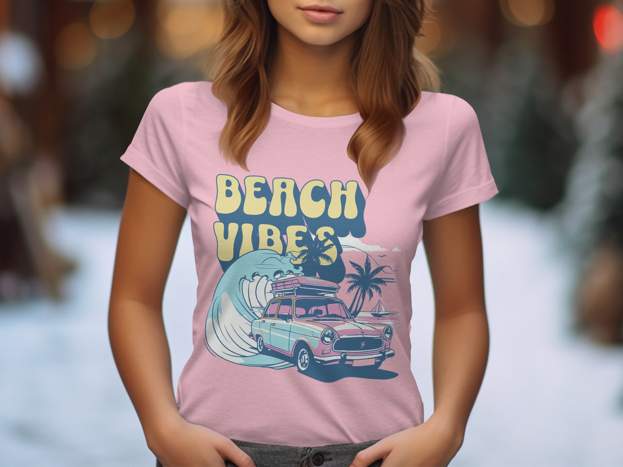 A woman is wearing a Garment Graphics pink retro T-shirt featuring a vintage car, large wave, and palm trees with Beach Vibes text. The softly blurred background has bokeh lights.