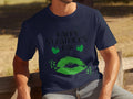 A person sits on a bench outside wearing a Garment Graphics navy blue St. Patricks Day T-shirt adorned with two green shamrocks and sparkling green lips, capturing the festive spirit perfectly.