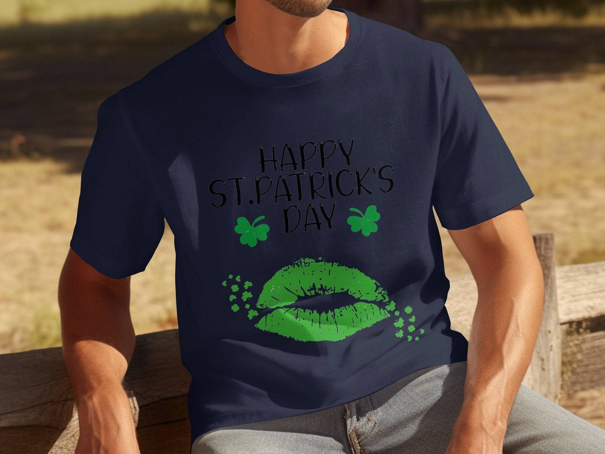 A person sits on a bench outside wearing a Garment Graphics navy blue St. Patricks Day T-shirt adorned with two green shamrocks and sparkling green lips, capturing the festive spirit perfectly.