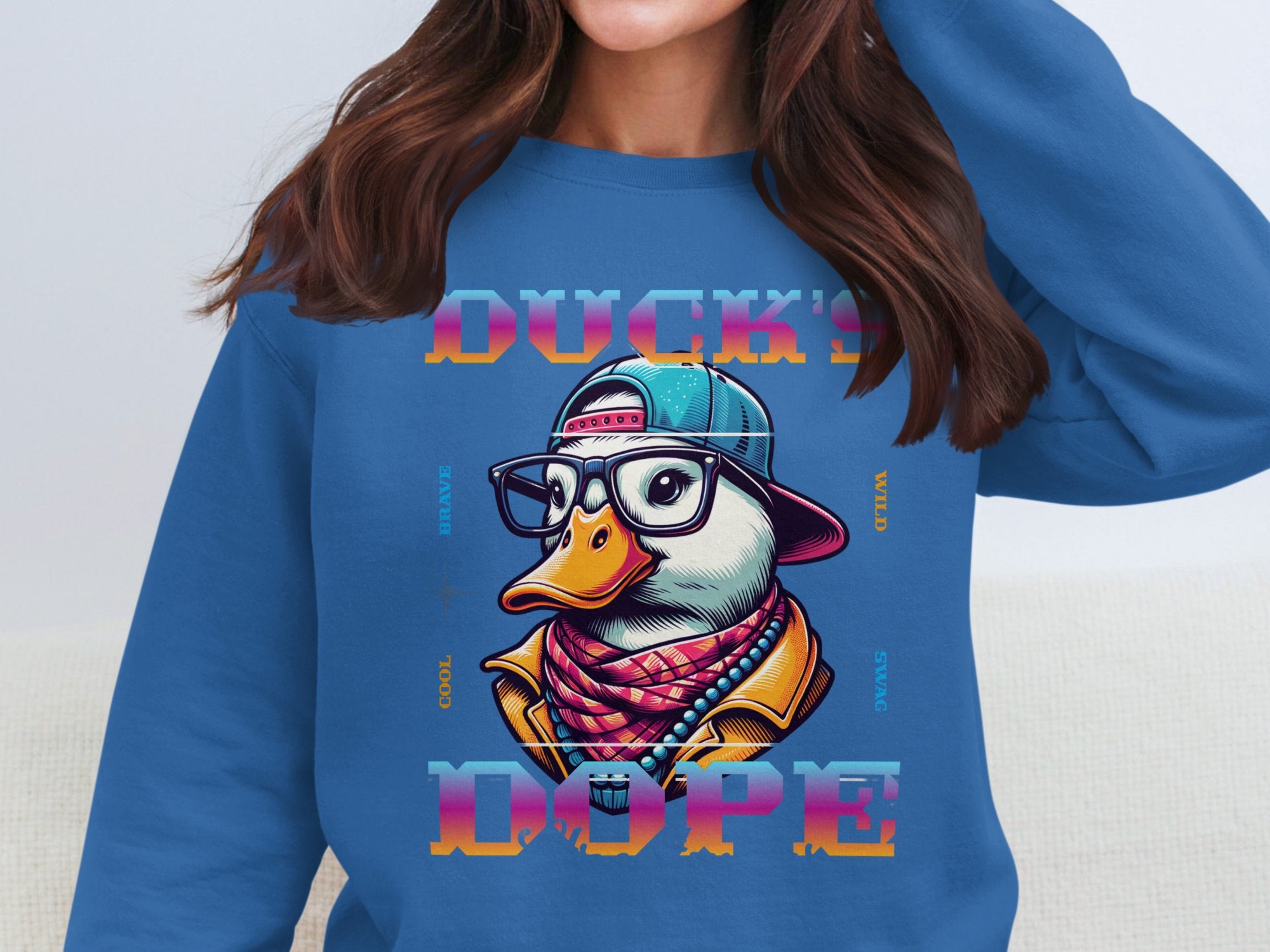 Wearing a stylish blue Garment Graphics sweatshirt, featuring a quirky duck with glasses, cap, and scarf. The bold fashion statement reads DUCKS DOPE, surrounded by words like COOL, BRAVE, WILD, and SPACE for a playful yet edgy vibe.