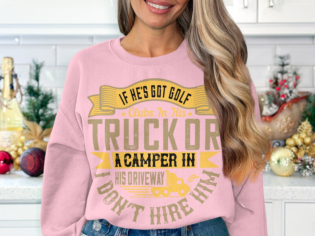A person in a humorous pink Garment Graphics sweatshirt that reads If hes got golf clubs in his truck or a camper in his driveway, dont hire him. stands in a kitchen decorated with holiday ornaments and small trees.