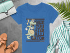 Garment Graphics presents a blue womens alligator t-shirt illustrating a smiling gator with a basketball and playful text See you later, alligator, displayed on gray with a purse, striped shirt, sandals, and fern leaf.