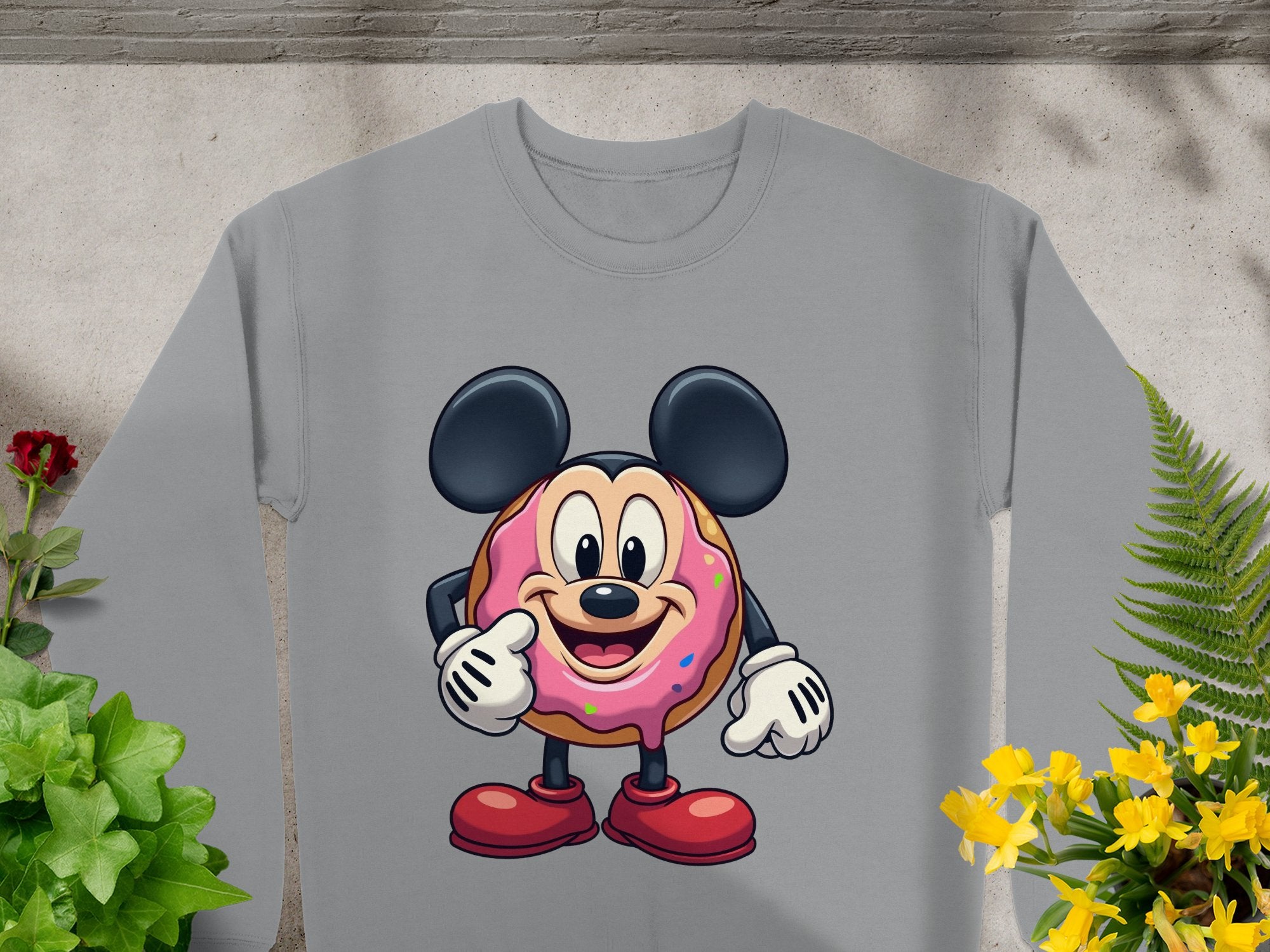 Garment Graphics presents a gray unisex sweatshirt featuring a playful donut character with mouse ears, gloves, and big shoes, pointing and smiling amid plants and yellow flowers.