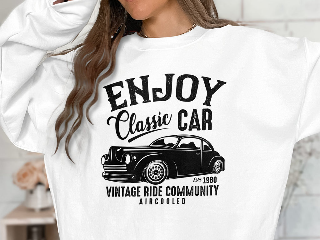 A person wears a Garment Graphics sweatshirt featuring a black classic car graphic. It reads ENJOY Classic CAR, Established 1980, and VINTAGE RIDE COMMUNITY AIRCOOLED. Their face isnt visible, emphasizing the designs timeless appeal.