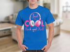Someone wearing a bright blue Garment Graphics t-shirt with Just be Cool Rock and Roll and pink white fun headphones around Cool displays their passion for rock and roll tees in a blurred modern room setting.