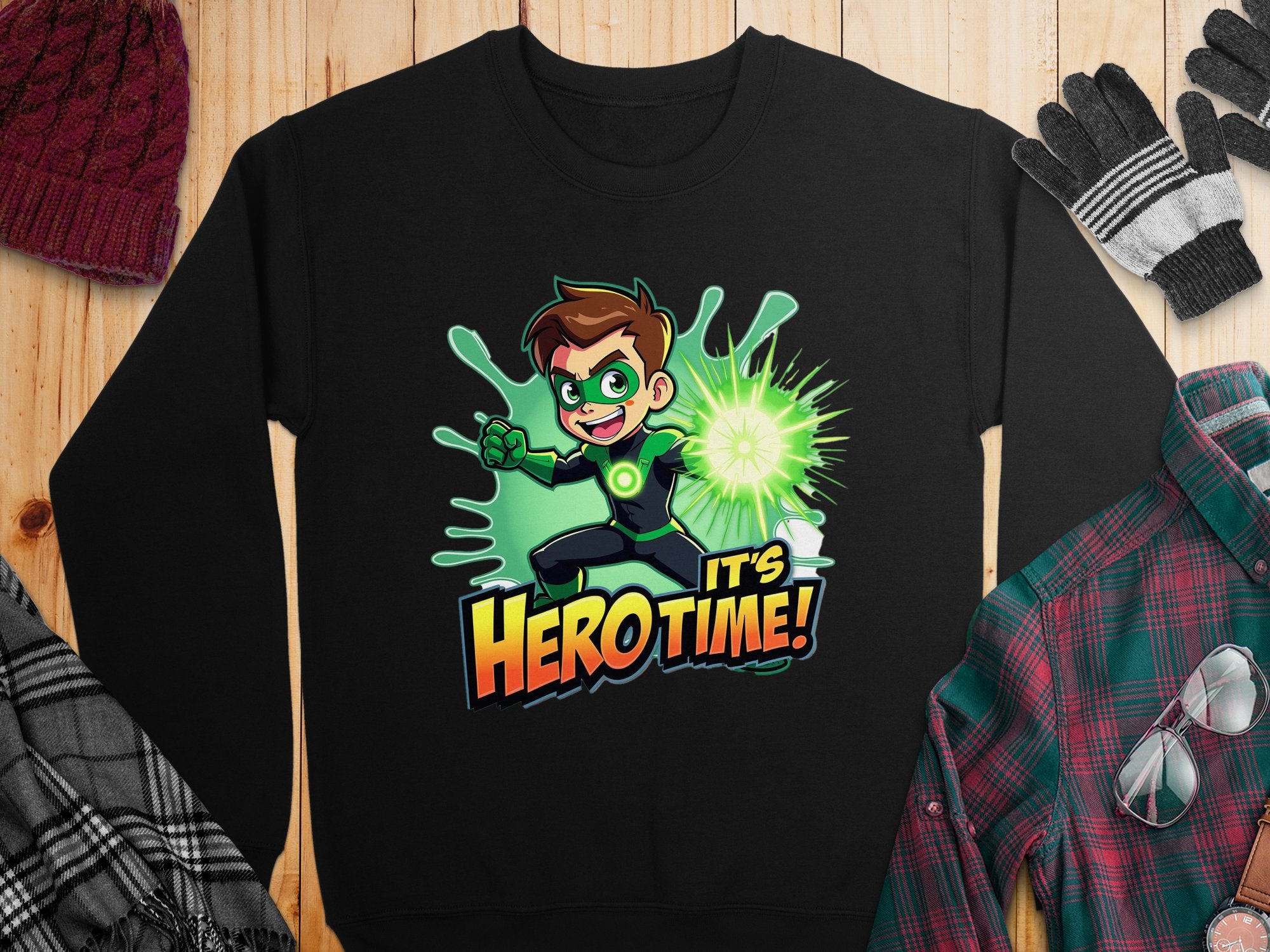 The black cartoon-themed sweatshirt from Garment Graphics features a superhero with brown hair in a green outfit, emitting green energy from a wrist device, and is completed with the phrase Its Hero Time!. Pair it with the nearby knit hat, gloves, and matching plaid shirt.