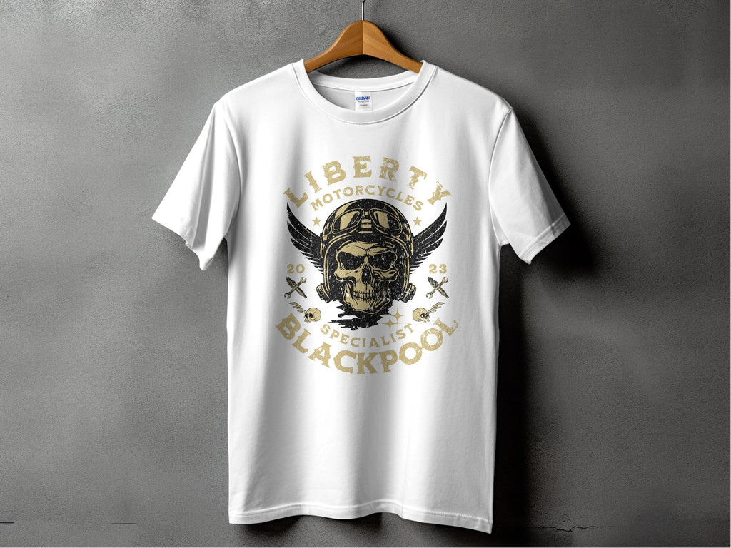 A white T-shirt by Garment Graphics on a wooden hanger against a gray backdrop, ideal for motorcycle fans. It features a vintage skull with goggles and wings, encircled by Liberty Motorcycles Specialist Blackpool 2023 and skull-and-crossbones icons.