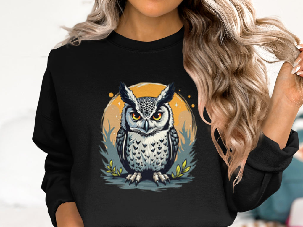 A person with wavy blonde hair wears a Garment Graphics black unisex sweatshirt, featuring an owl with an intense gaze against an orange circle, decorated with grass and small leaves.