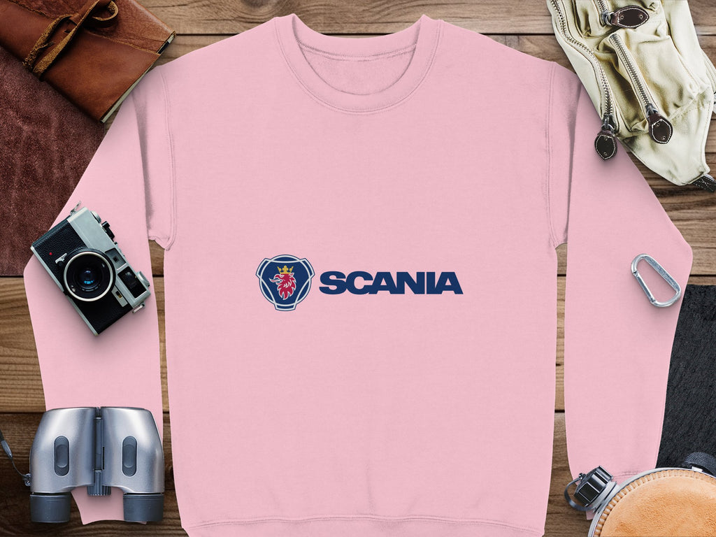 A Garment Graphics unisex pink sweatshirt with the iconic Scania logo and griffin head, displayed on wood. Perfect for casual outings, its accompanied by a camera, binoculars, leather bag, watch, and carabiner.