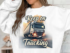A person wearing a Garment Graphics unisex graphic sweatshirt features a large truck with headlights and the text Keep On Trucking above and below it. Only their torso is visible, as they are partially out of frame.