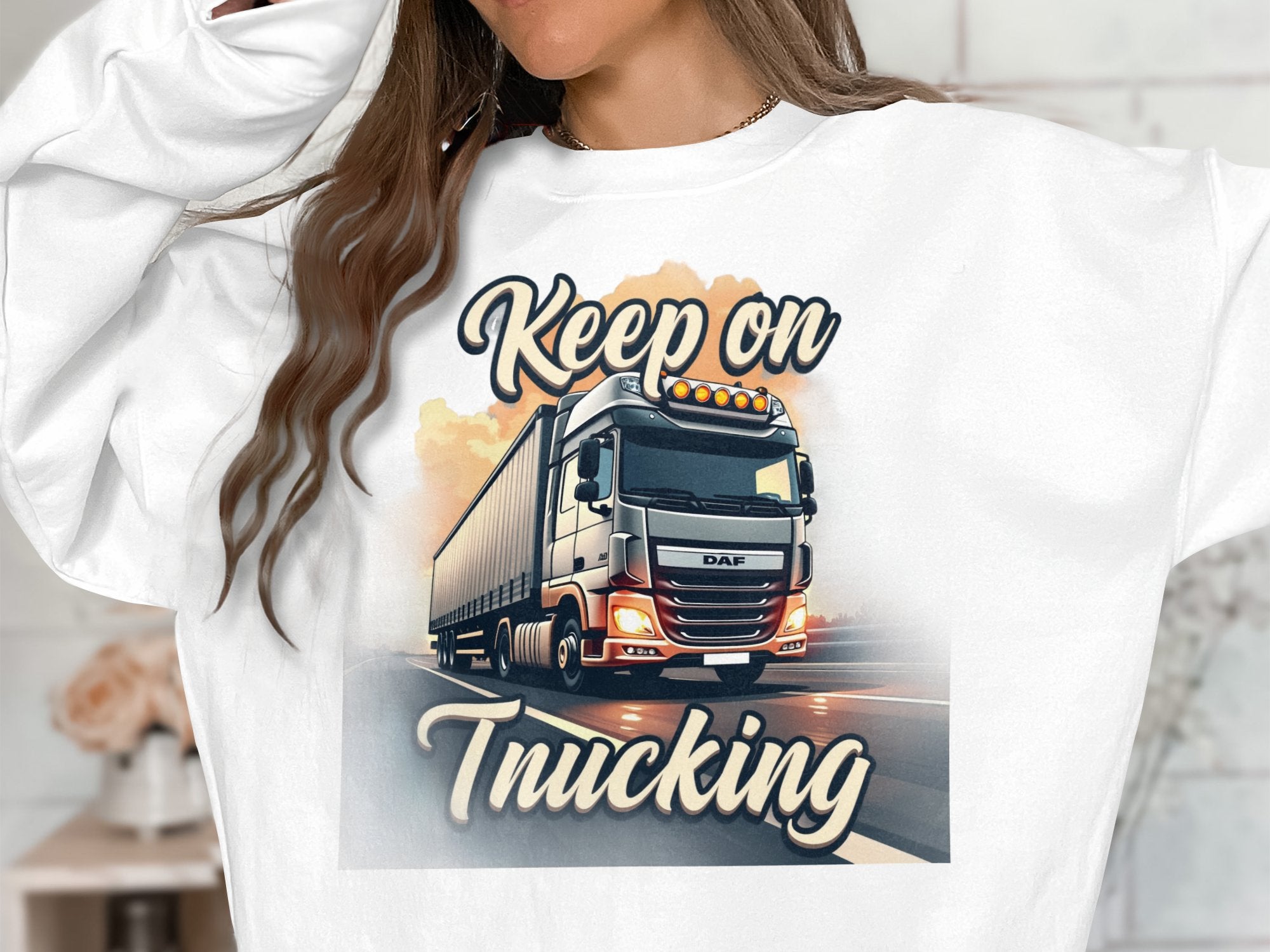 A person wearing a Garment Graphics unisex graphic sweatshirt features a large truck with headlights and the text Keep On Trucking above and below it. Only their torso is visible, as they are partially out of frame.