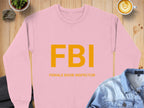 Versatile unisex pink sweatshirt from Garment Graphics with bold yellow FBI and FEMALE BOOB INSPECTOR text. Its styled on a wooden surface, complemented by a denim shirt and a latte in the top right corner.