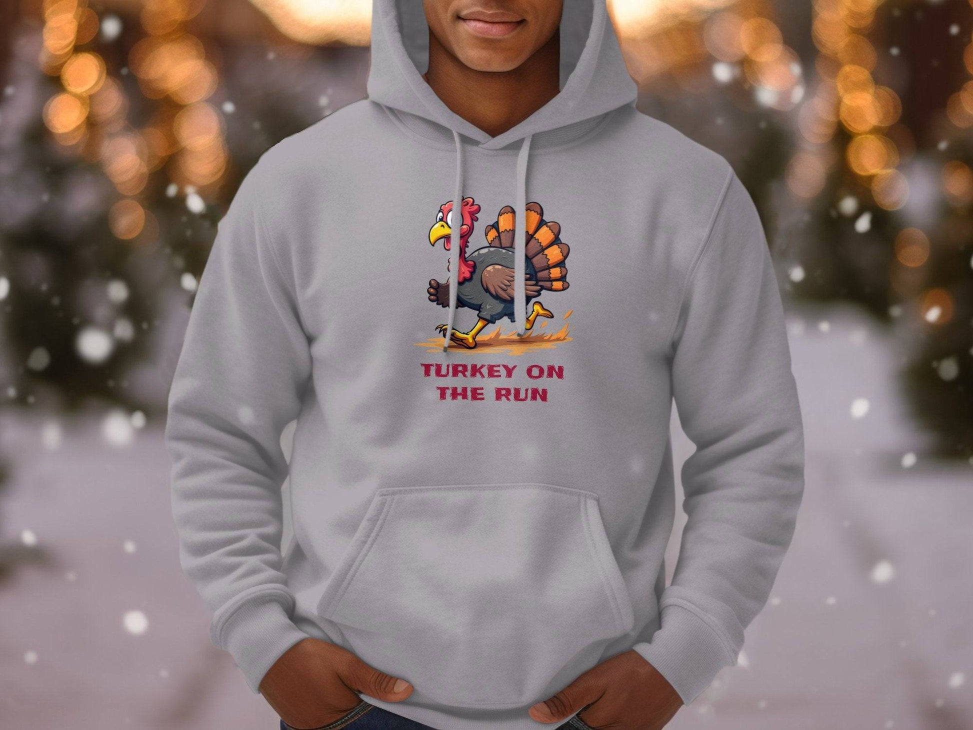 In a snowy setting with blurred tree lights, someone wears a quirky Garment Graphics hoodie featuring a cartoon turkey and the catchy phrase Turkey On The Run.