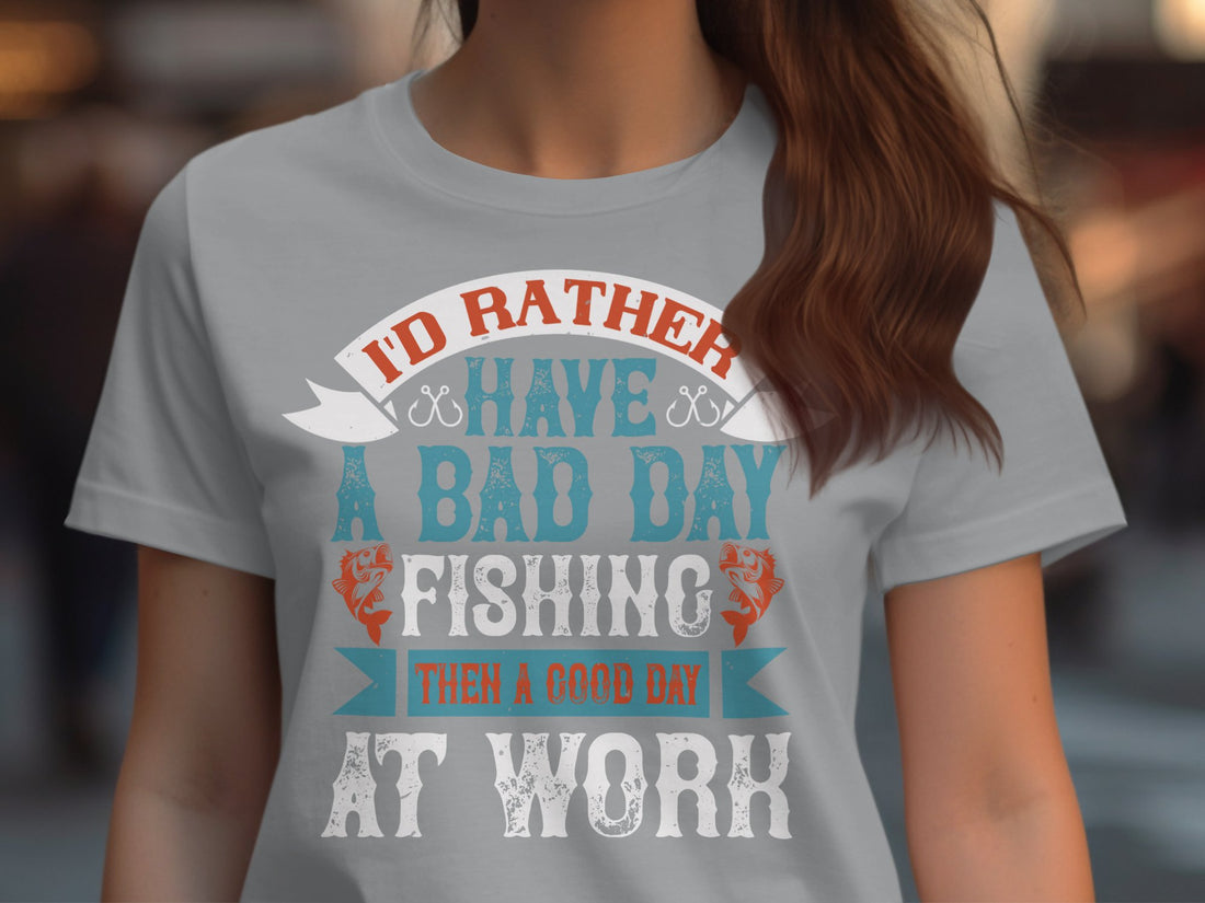 A Garment Graphics white fishing T-shirt with the words Id rather have a bad day fishing than a good day at work is displayed on wood. Its surrounded by gifts, pine cones, a sweater, an ornament, and berries. Available in womens sizes, its perfect for fishing fans.