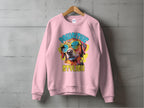 A light pink Dog Graphic Sweatshirt by Garment Graphics hangs against a concrete wall, featuring a vibrant image of a sunglasses-wearing canine. The words Pawsitive Stylish artistically frame the design, perfect for true dog lovers.