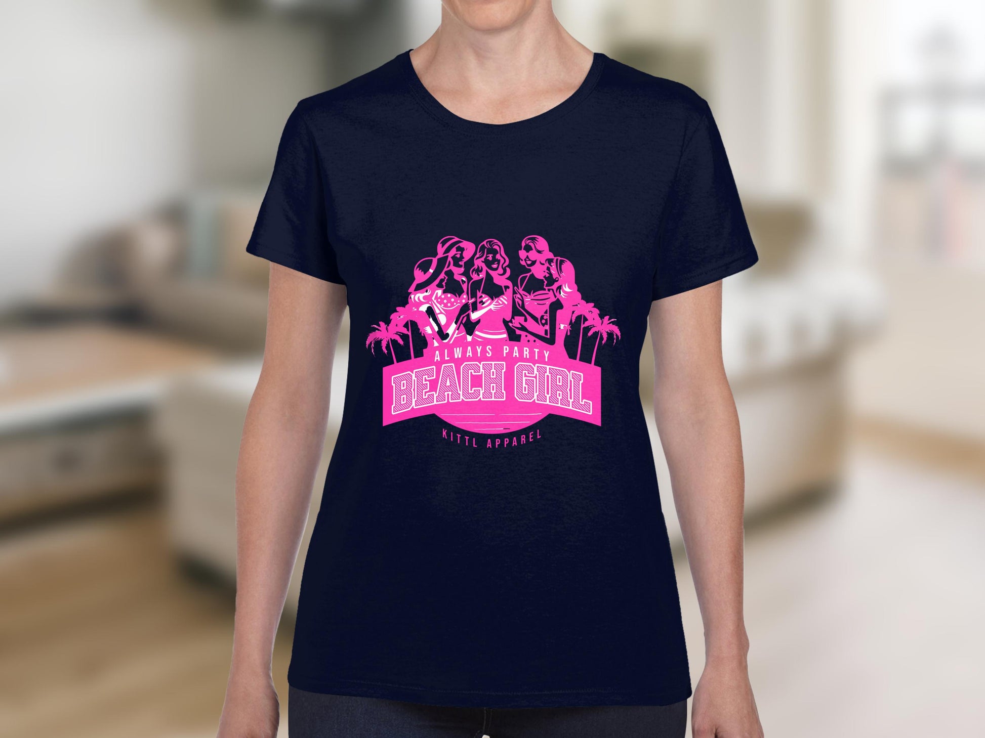 Dressed in a navy blue t-shirt by Garment Graphics, adorned with a pink graphic of three women and palm trees, the text Always Party Beach Girl, Kite Apparel stands out. This stylish womens semi-fitted tee suits anyone who loves Always Party Apparel. A blurred indoor setting forms the background.