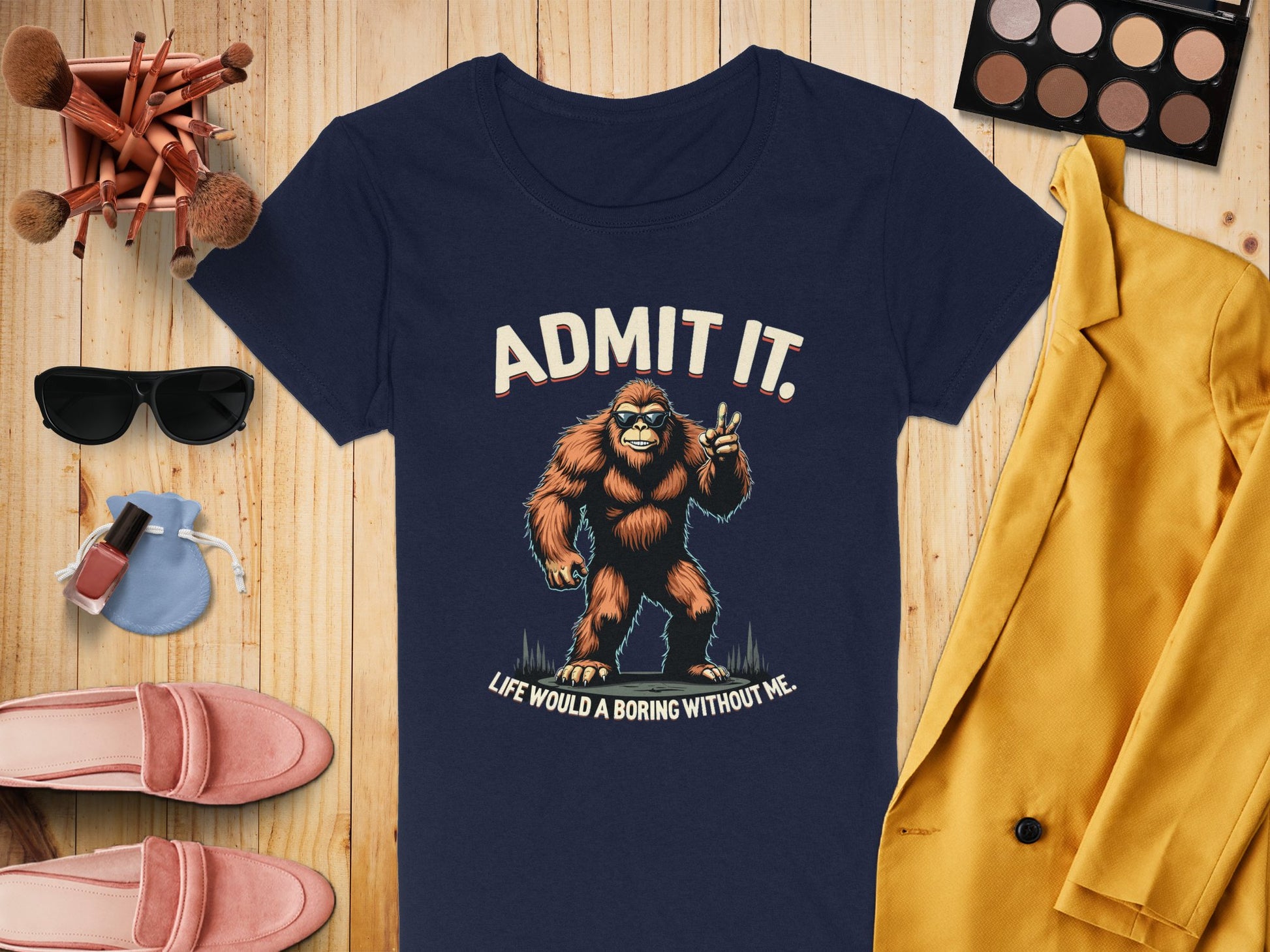 A navy Garment Graphics T-shirt with ADMIT IT BIGFOOT. LIFE WOULD BE BORING WITHOUT ME. pairs well with makeup brushes, eyeshadow, sunglasses, nail polish, pink loafers, a yellow blazer, and denim jeans. Ideal for quirky T-shirt enthusiasts!.