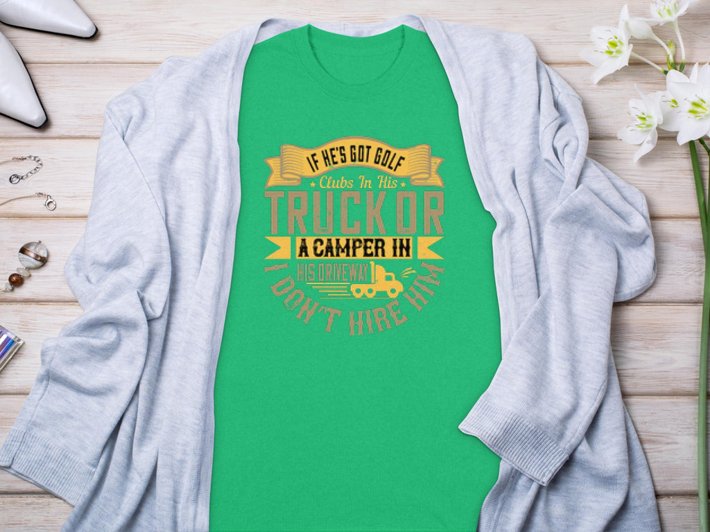 A Garment Graphics green t-shirt featuring the witty design If hes got golf clubs in his truck or a camper in his driveway... dont hire him is displayed on a wooden surface, accented by a gray cardigan, flowers, and accessories. Ideal for both camping and golf fans.
