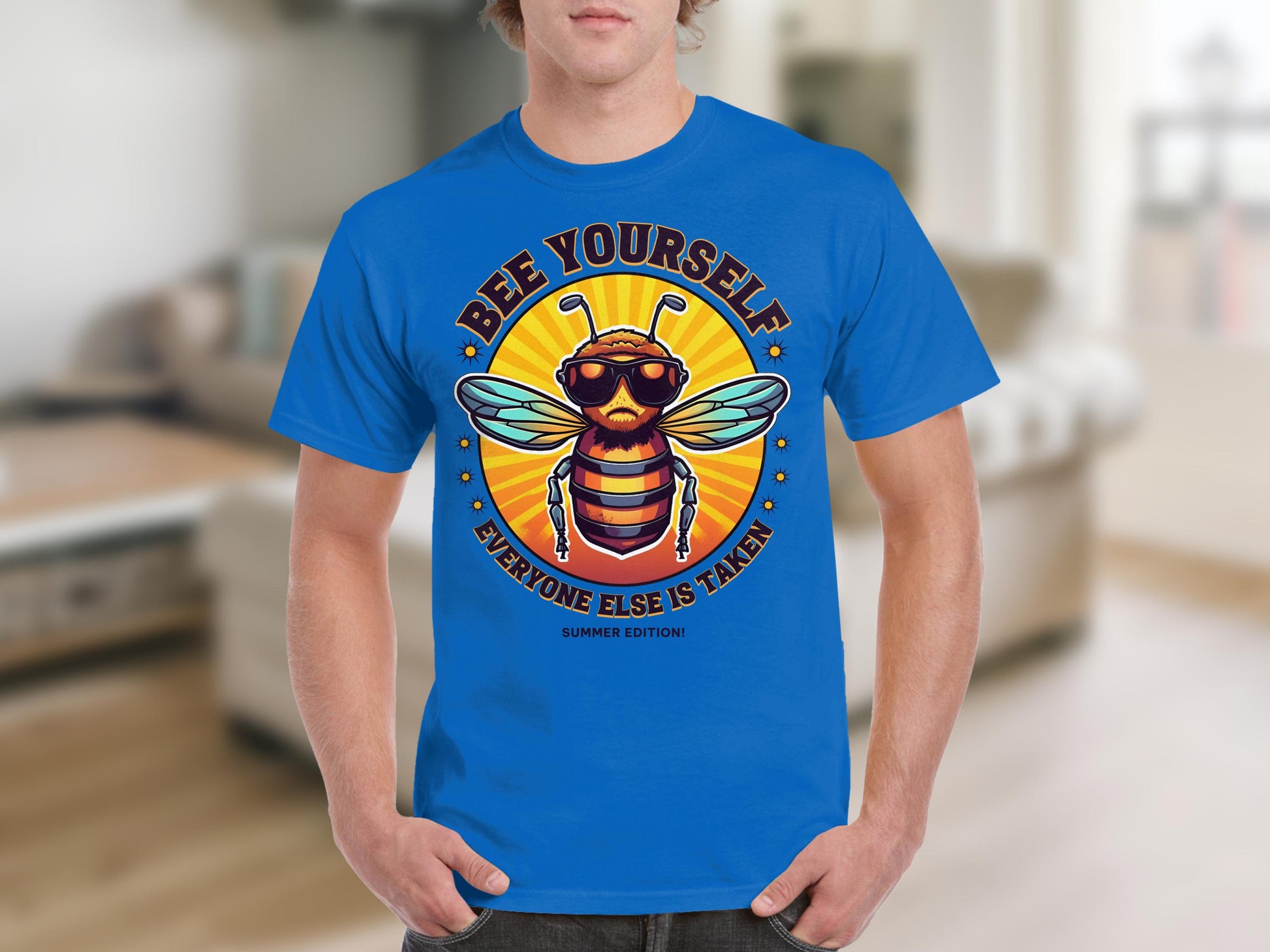 A person dons a blue T-shirt by Garment Graphics, showcasing a stylish bee with sunglasses. The shirt reads Bee Yourself, Every One Else Is Taken, Summer Edition. Its ideal for family sizing against a blurred indoor backdrop.