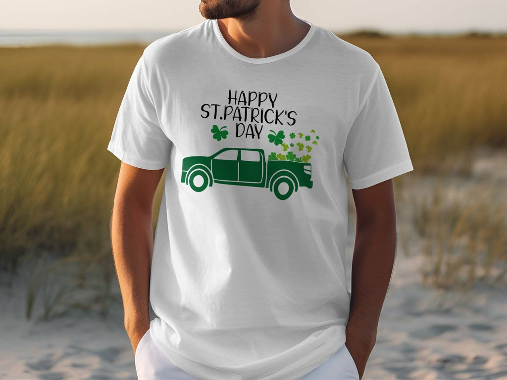 Someone sports a Garment Graphics white T-shirt featuring a green pickup truck filled with shamrocks. The shirt reads Happy St. Patricks Day, celebrating Irish pride, set against a grassy field backdrop.