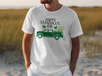 Someone sports a Garment Graphics white T-shirt featuring a green pickup truck filled with shamrocks. The shirt reads Happy St. Patricks Day, celebrating Irish pride, set against a grassy field backdrop.