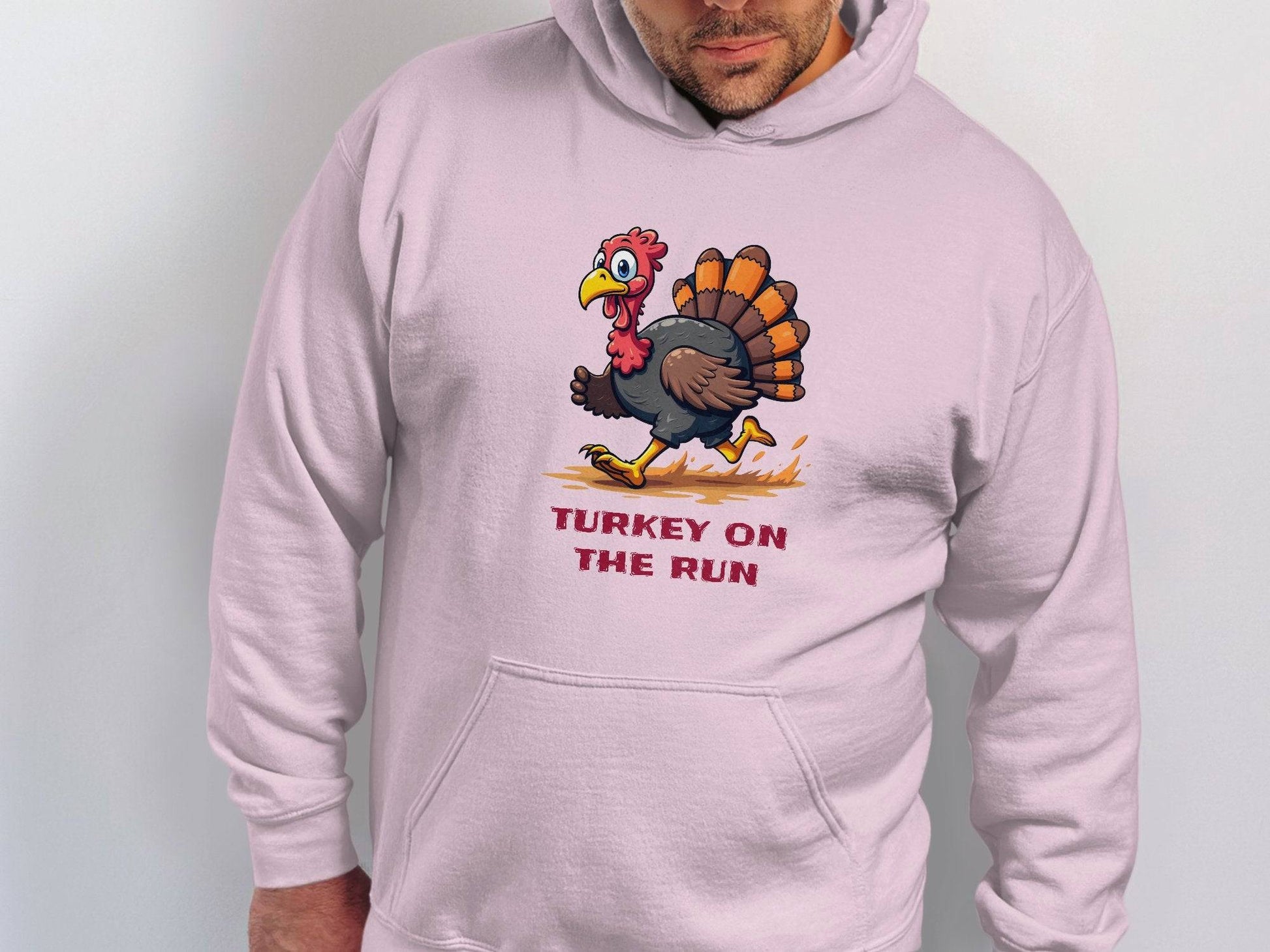 Wearing a light hoodie by Garment Graphics, someone shows off a cartoon turkey sprinting with orange speed lines. Under the lively graphic, bold text reads TURKEY ON THE RUN.