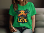 Wearing a green t-shirt with a tropical sunset design featuring two palm trees, a flying bird, and One Love on the front from Garment Graphics, a person relaxes on the couch—ideal for any beach outing.