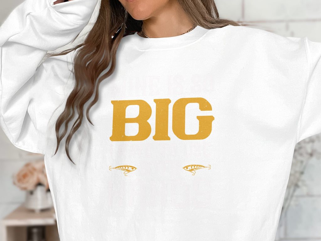 The individual wears a standout Garment Graphics sweatshirt displaying BIG in bold yellow letters, accompanied by two stylized eye graphics. Their long brown hair partially hides their face, enhancing the intrigue of this striking statement piece.