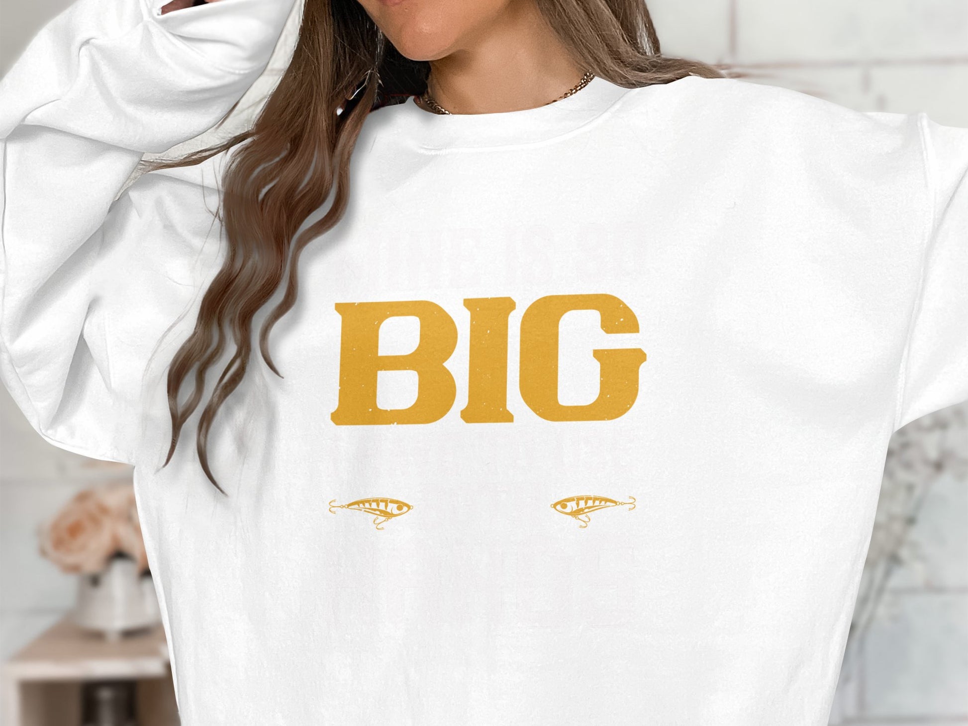 The individual wears a standout Garment Graphics sweatshirt displaying BIG in bold yellow letters, accompanied by two stylized eye graphics. Their long brown hair partially hides their face, enhancing the intrigue of this striking statement piece.