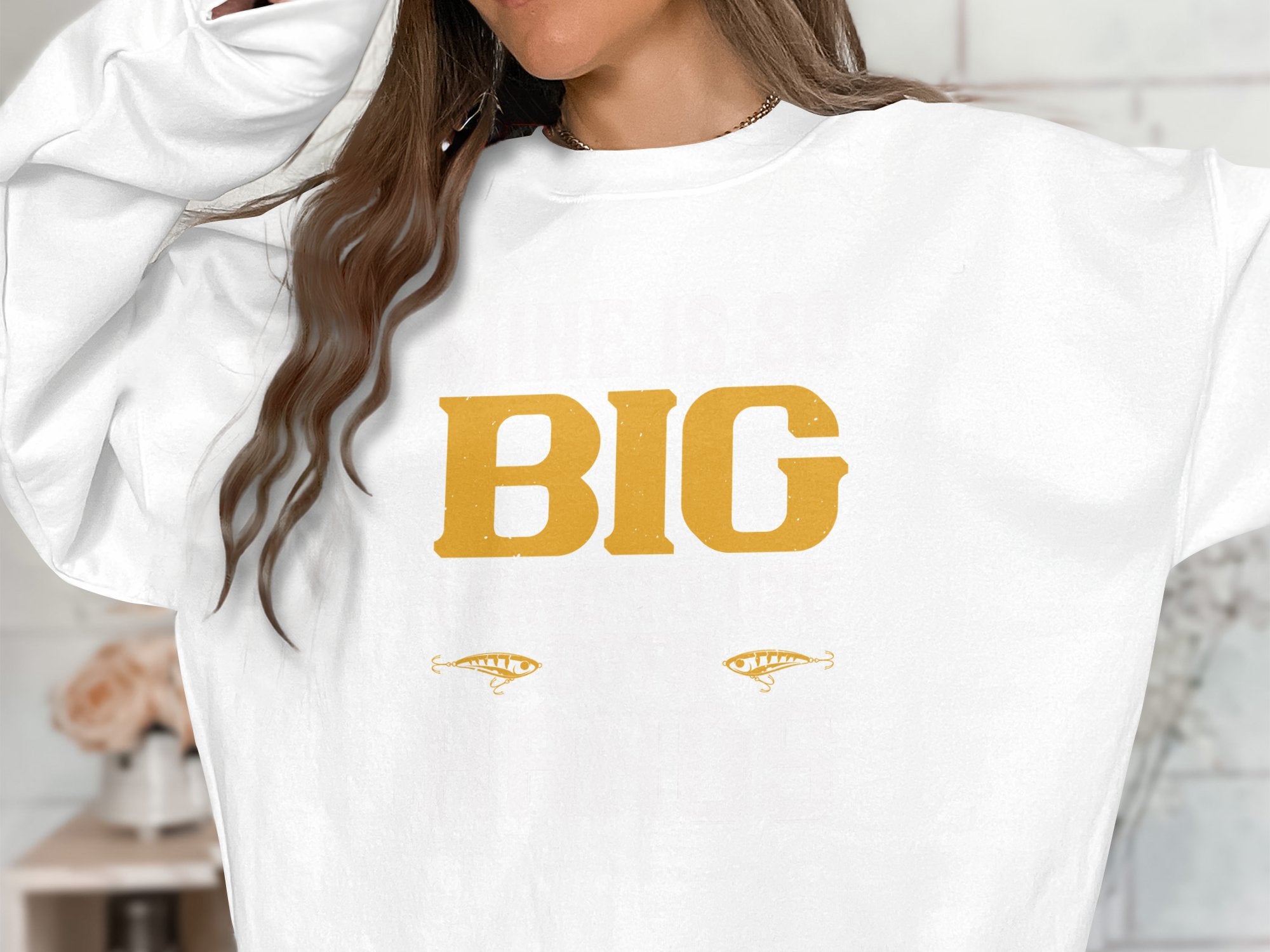 The individual wears a standout Garment Graphics sweatshirt displaying BIG in bold yellow letters, accompanied by two stylized eye graphics. Their long brown hair partially hides their face, enhancing the intrigue of this striking statement piece.