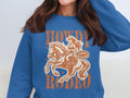 A person in a Garment Graphics Howdy Rodeo Sweatshirt features a cowgirl on horseback with bold orange letters Howdy Rodeo and Not a Beginner, perfectly embodying the cowboy spirit. The persons face is not visible, making it appealing to rodeo enthusiasts everywhere.