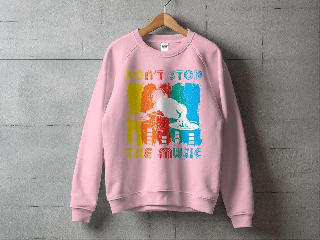 A pink Garment Graphics DJ sweatshirt, perfect for music lovers, hangs on a concrete wall. It features colorful graphics with a DJ silhouette at turntables and the phrase DONT STOP THE MUSIC, in blue, red, yellow, and white accents. Available in unisex sizing.