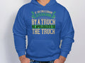 A person sports a Garment Graphics blue hoodie with a humorous quote in green and white that reads, If an Englishman gets run down by a truck, he apologizes to the truck, adorned with decorative elements enhancing its charm.