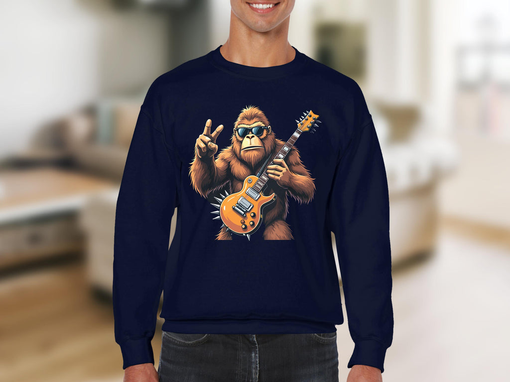 A person in a dark blue Garment Graphics sweatshirt features a gorilla playing an electric guitar. The sunglasses-wearing gorilla, flashing a peace sign, pops against a blurred indoor backdrop—ideal for music enthusiasts.